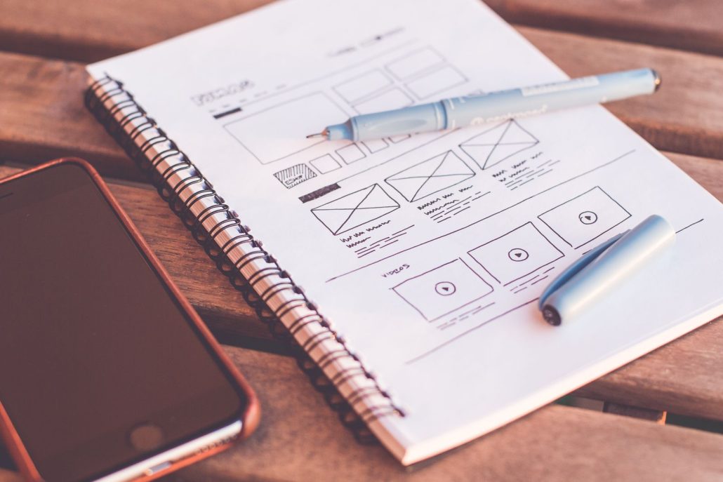 App wireframe sketches in a notebook beside a smartphone, the storyboard that makes voice over for mobile app narration land