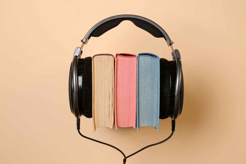 Headphones resting on books, the long-form listen audiobook narration has to hold from page 1 to page 300